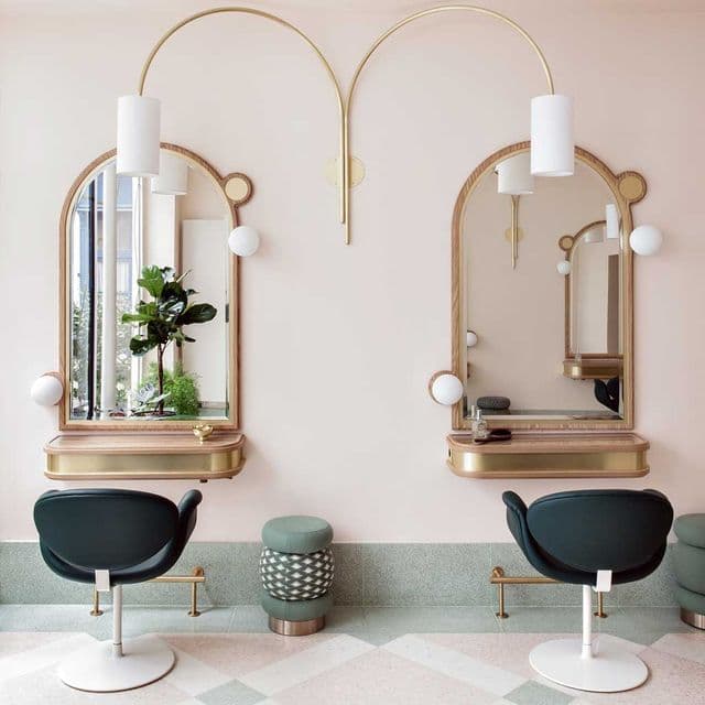 Deux postes de coiffure équipés de miroirs arqués et de fauteuils, dans un salon.